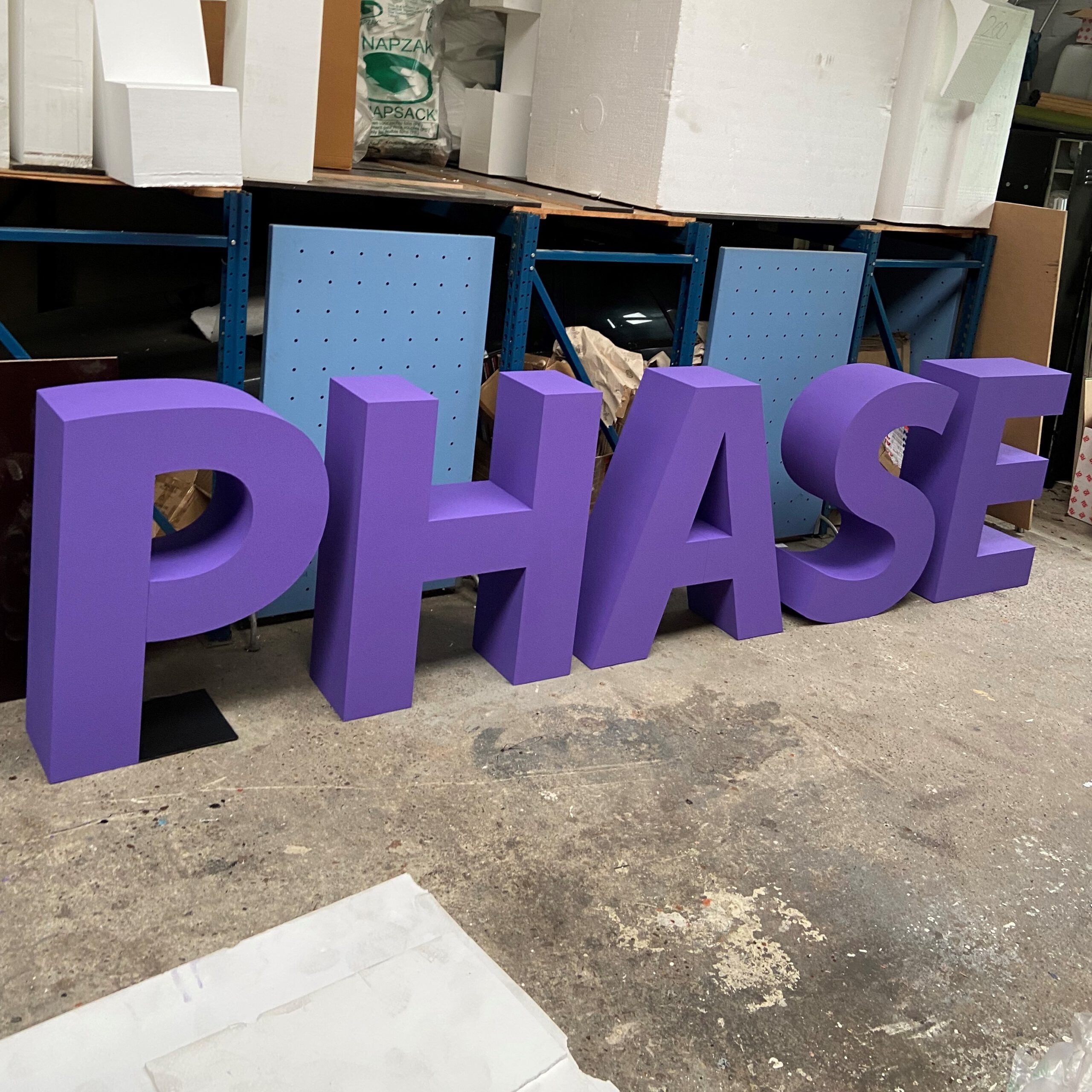 Large purple letters spelling 'PHASE' in a warehouse setting.