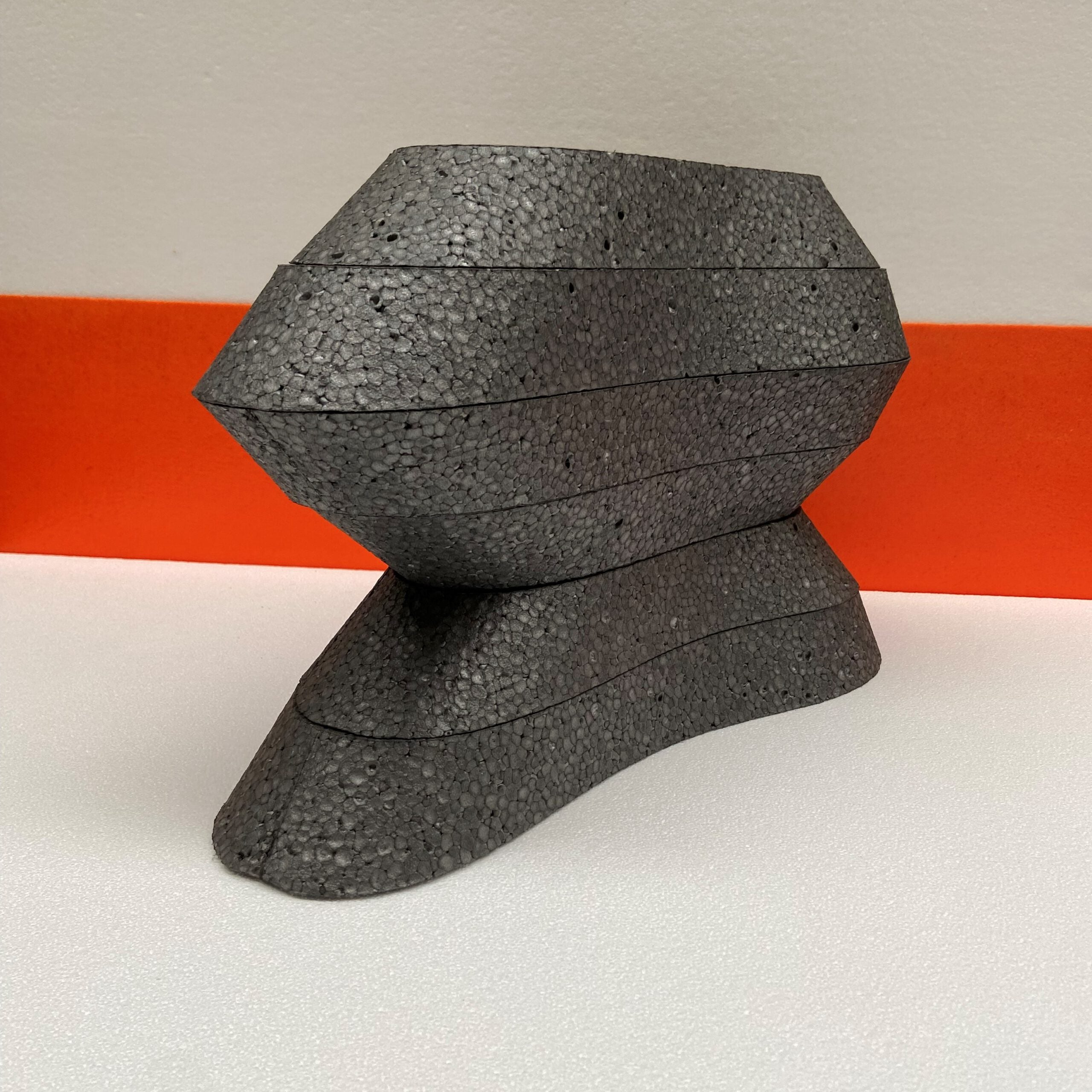 Geometric stone sculpture on a white and orange striped background