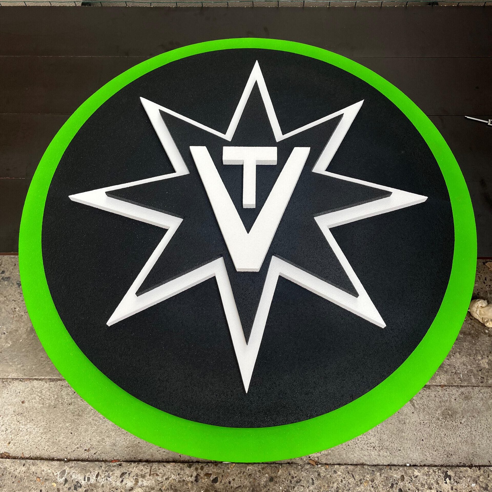 Logo with a white star and 'TV' initials on a black background with a green border, mounted on a wall.