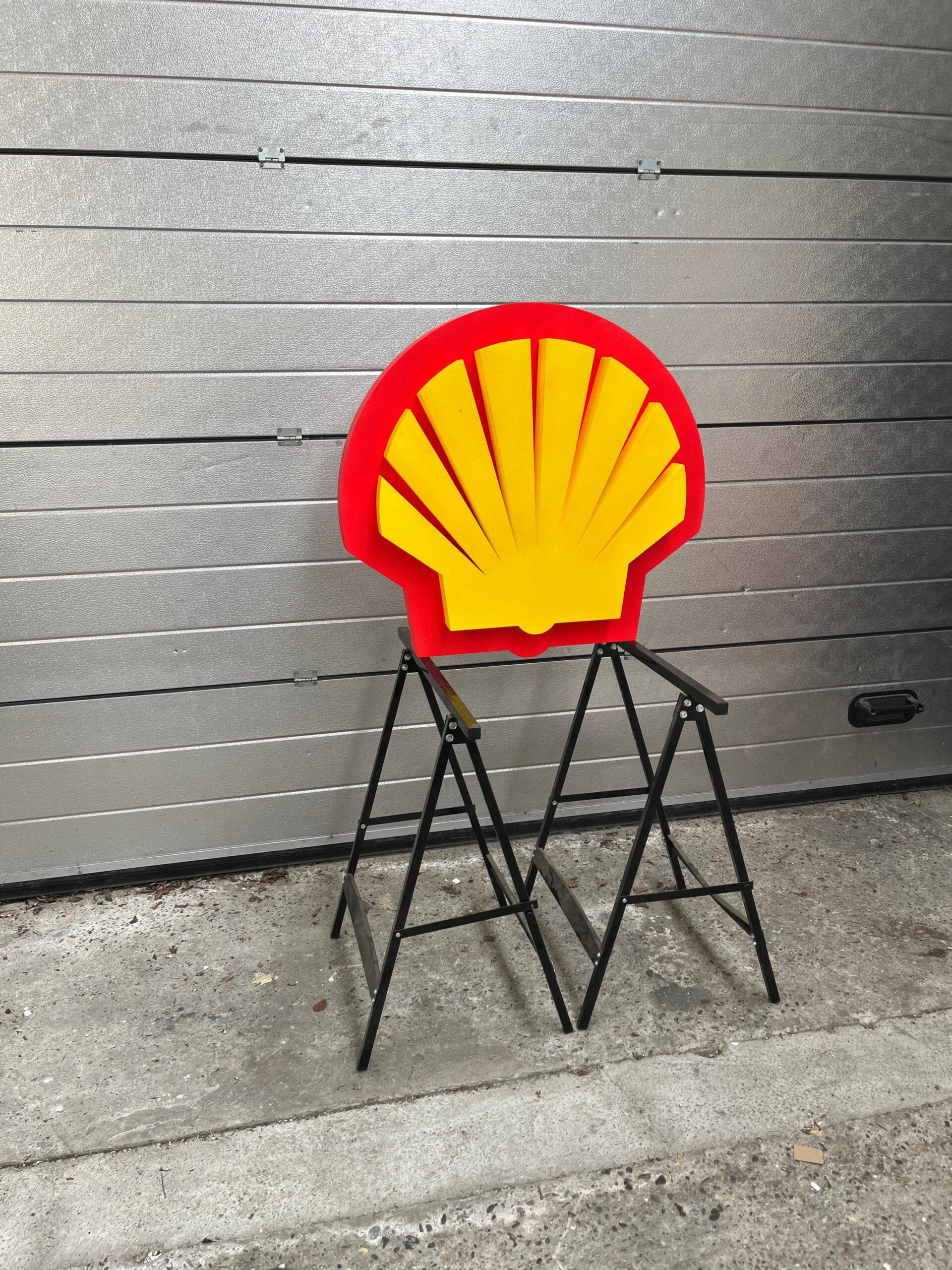 Shell logo on a step stool against a metallic wall.